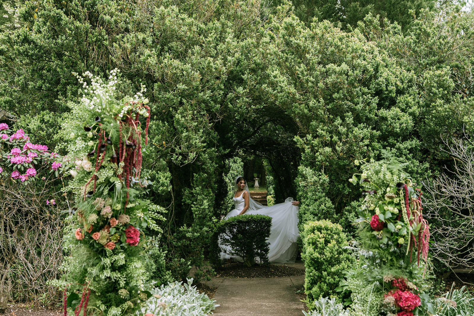 A bride walking through a hedge archway in a summer garden