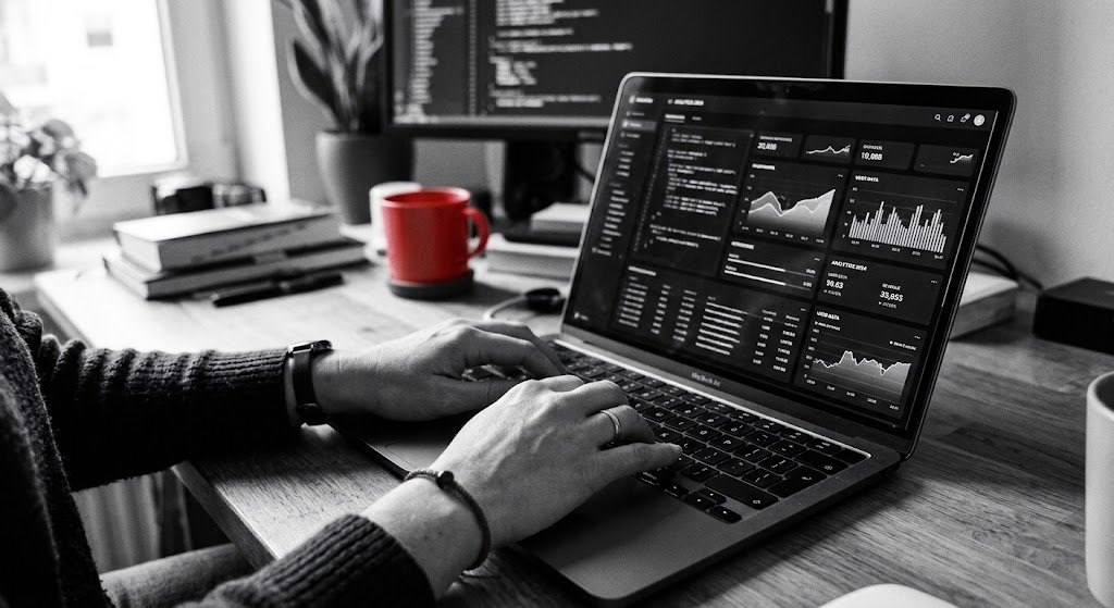 Mani al lavoro su un laptop con una dashboard di dati, accanto una tazza rossa