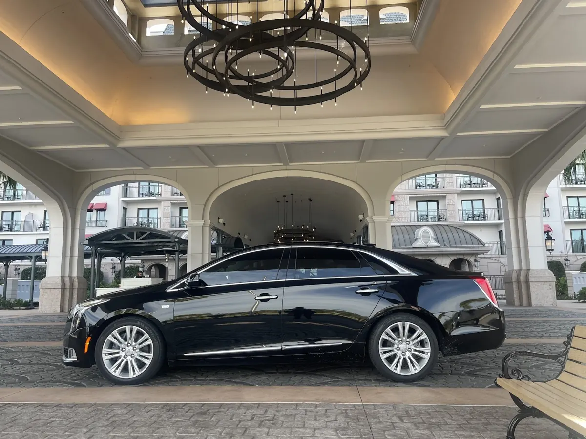 Black Cadillac sedan under a hotel entrance canopy with a chandelier