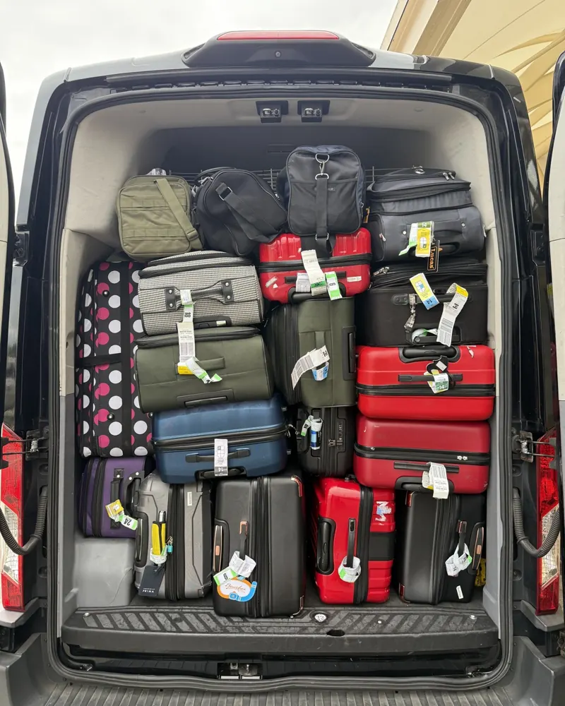 Passenger van with its rear doors open, packed floor to roof with suitcases