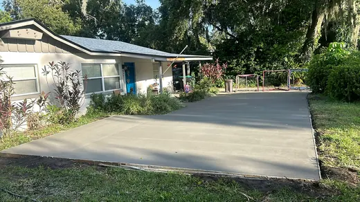 New concrete driveway leading up to a white house under oak trees