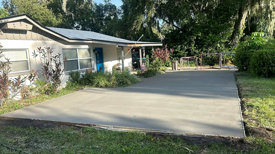 New concrete driveway leading up to a white house under oak trees