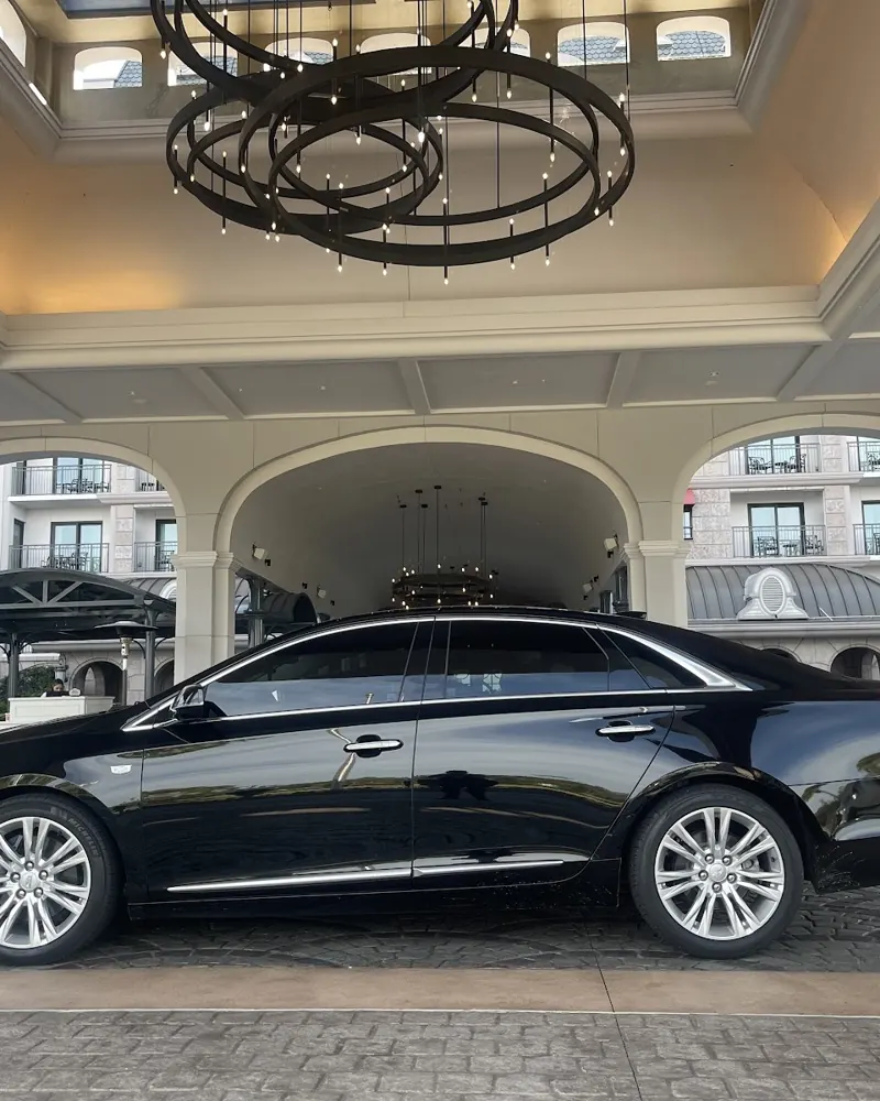 Black Cadillac sedan under a hotel entrance canopy with a chandelier