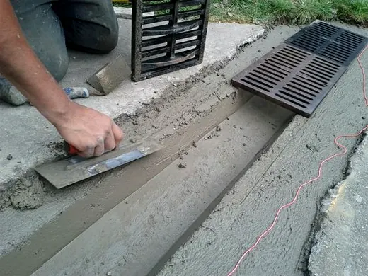Finisher smoothing fresh concrete with a trowel next to a drain grate
