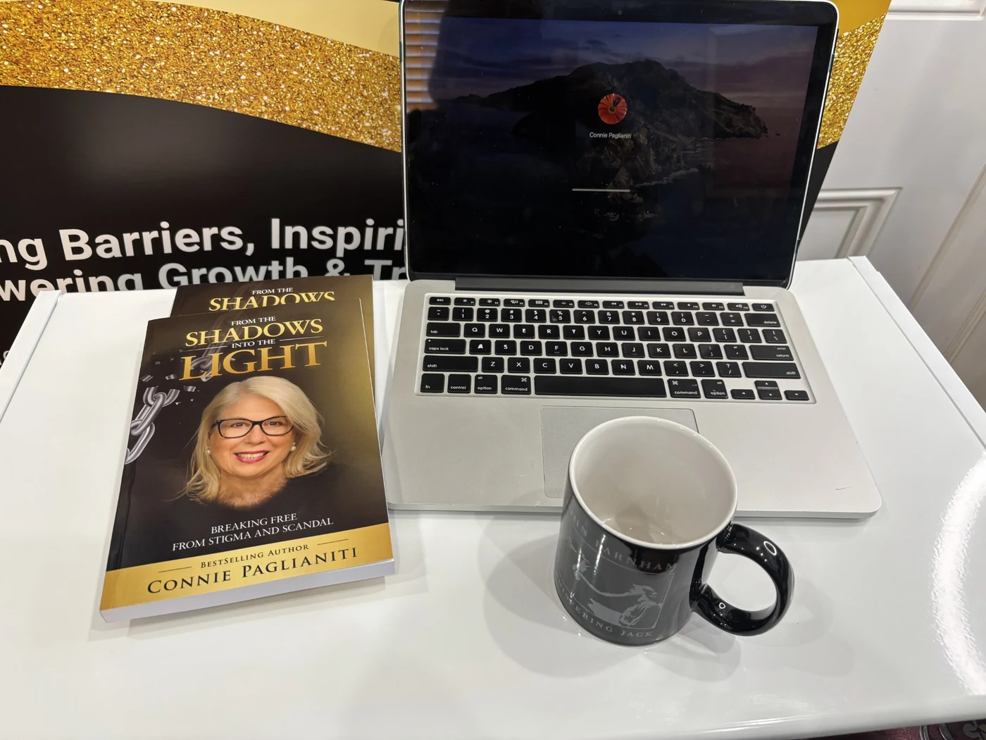 Copies of From the Shadows into the Light beside a laptop and coffee