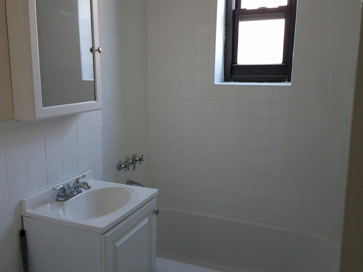 A small, freshly renovated bathroom with clean white tiles, a sleek white vanity, and a simple, modern design.