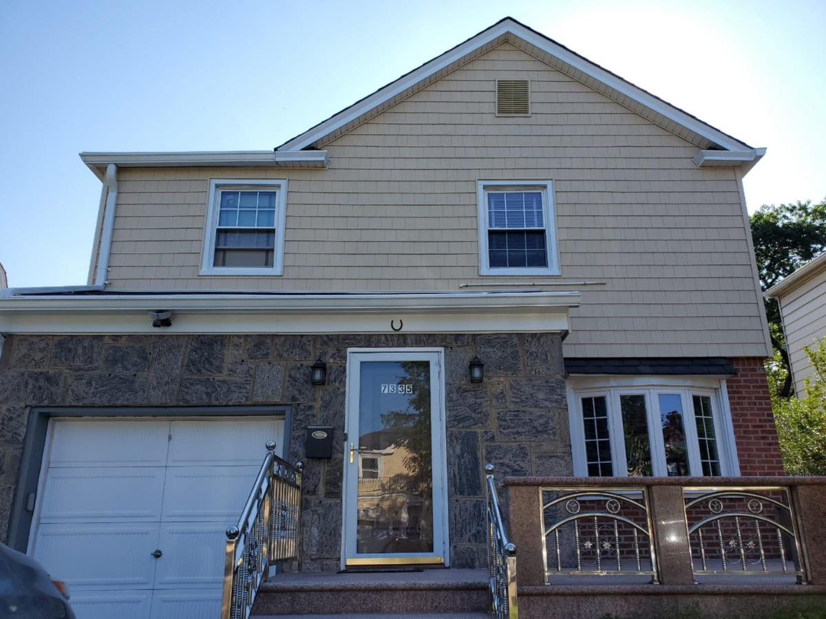 A home with a striking front facade featuring light-colored vinyl siding, stonework around the entrance, and a well-kept front yard.