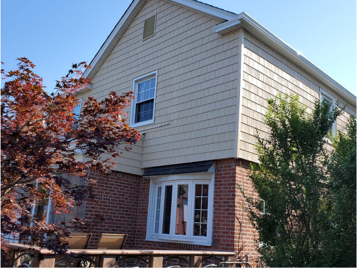 Side view of a home with fresh waterproofing and beige siding, surrounded by lush landscaping.