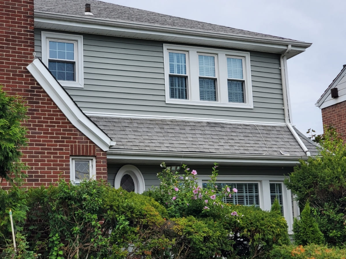 A home with a modern combination of gray vinyl siding and red brick, featuring new windows and well-maintained landscaping.