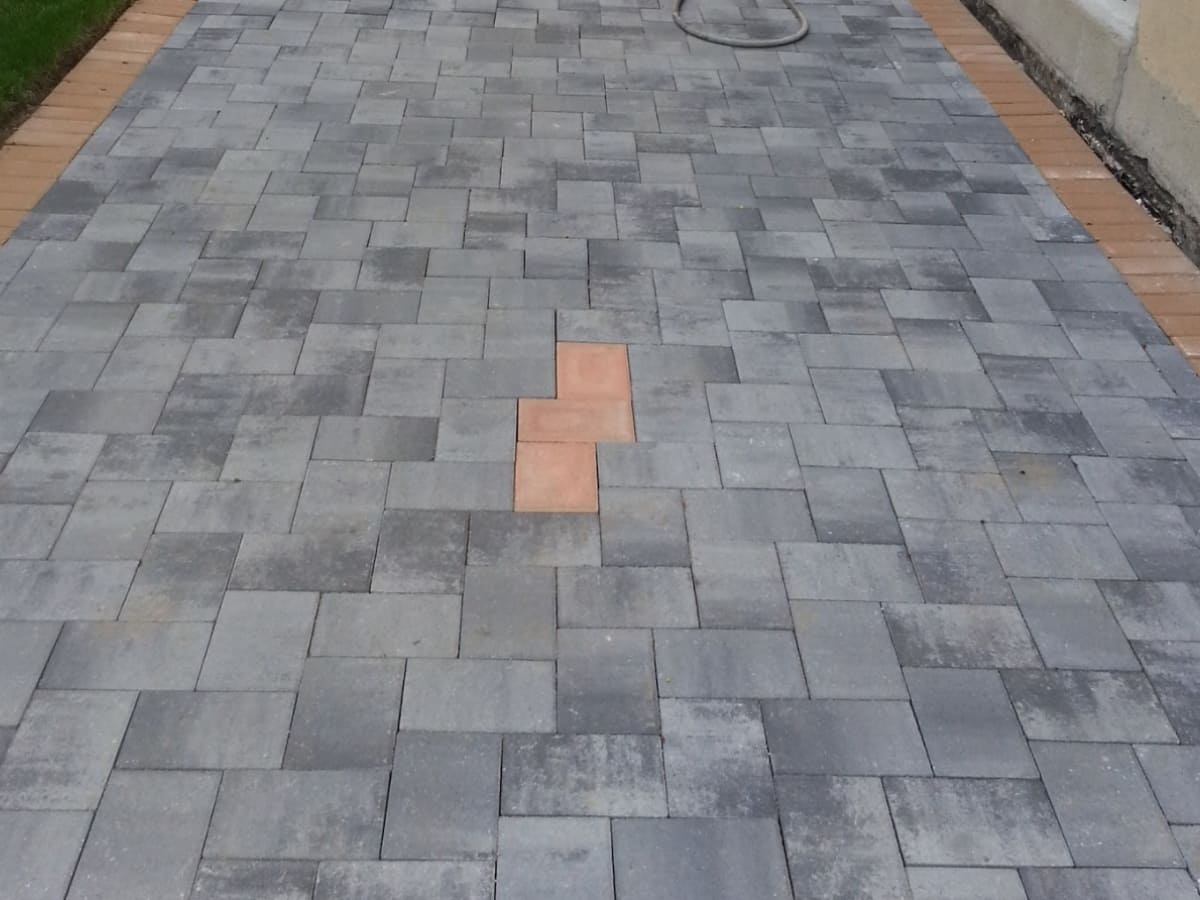 A modern driveway constructed with interlocking gray pavers, featuring a distinctive design with a contrasting brick pattern in the center.