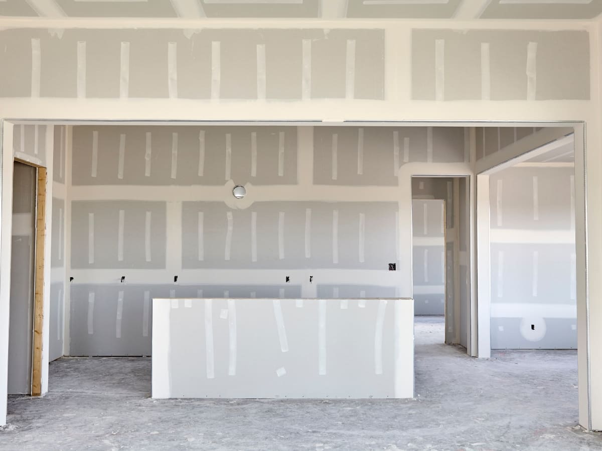 n interior view of a home under construction, featuring freshly taped drywall in an open-concept space.