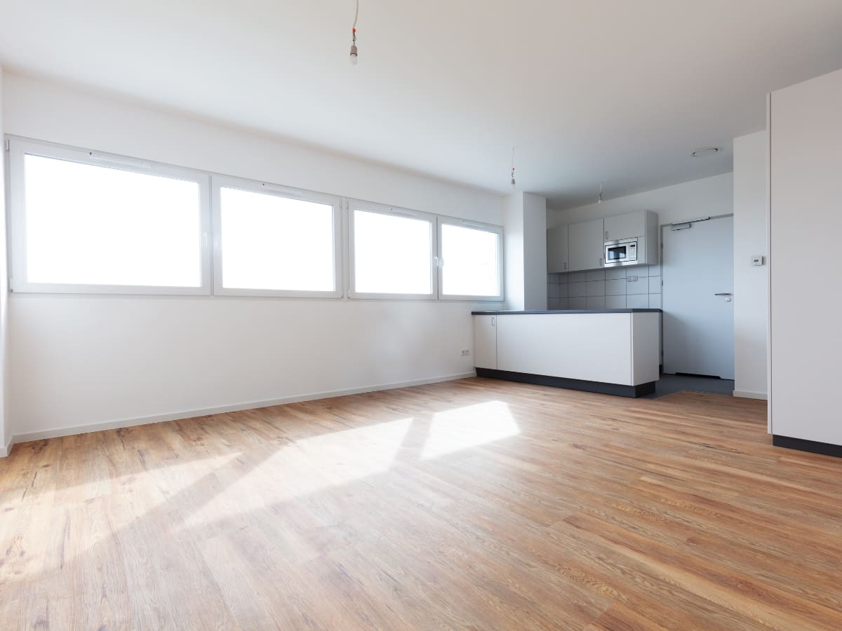 Spacious living area with waterproofed vinyl flooring, large windows, and a minimalistic kitchen.