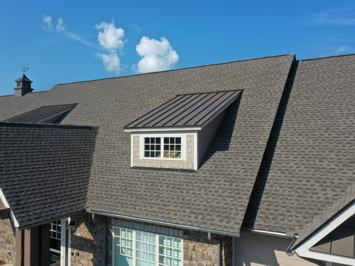 Aerial view of a newly installed shingle roof with a small dormer window, showcasing the completed weatherproofing and precise alignment of the shingles.