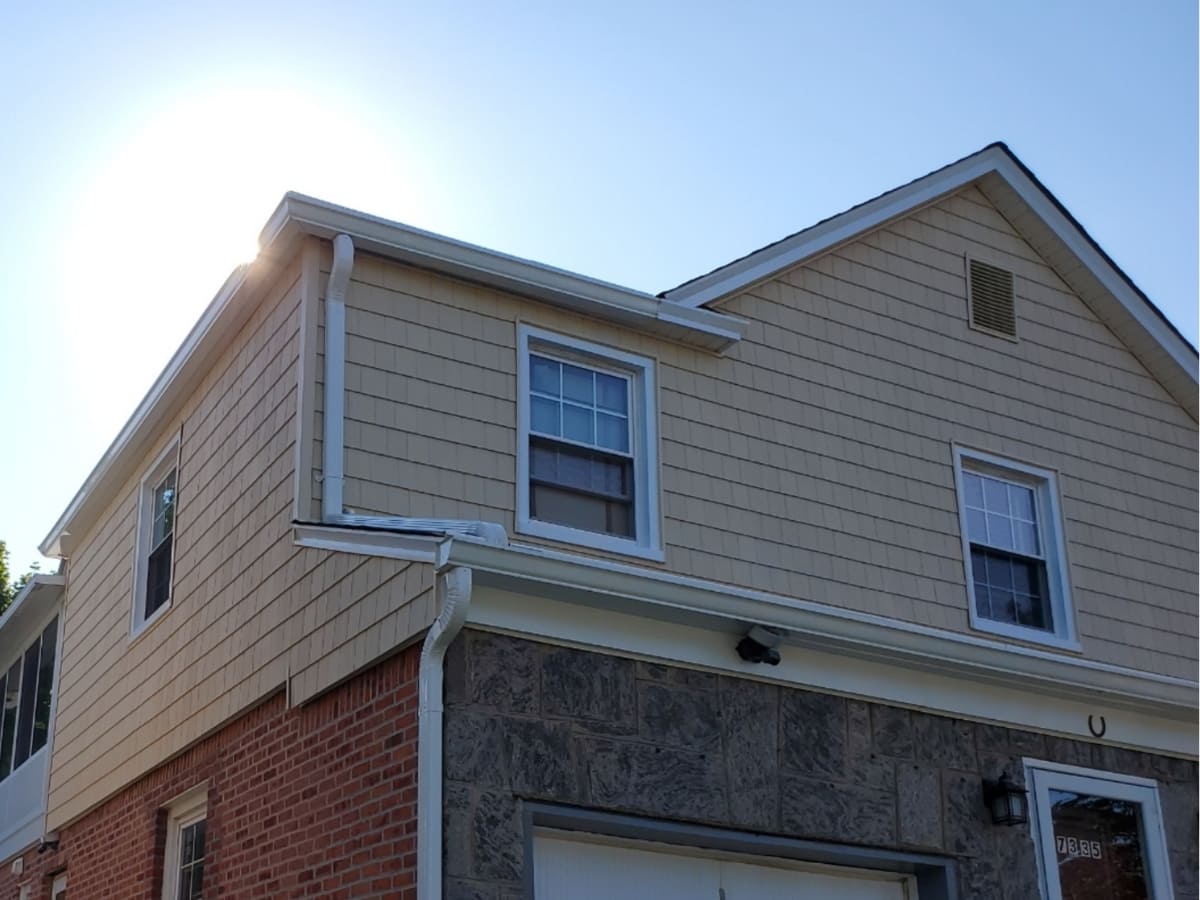 Sun shining on a newly waterproofed home exterior with beige siding and a brick foundation.