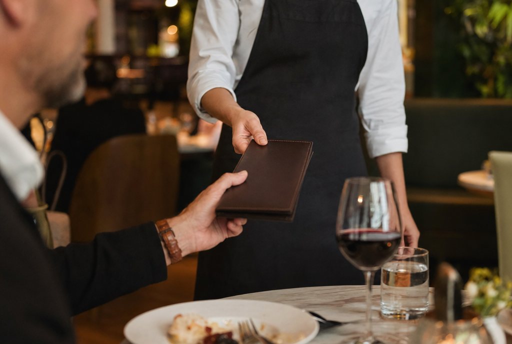 A server handing a check presenter to a guest