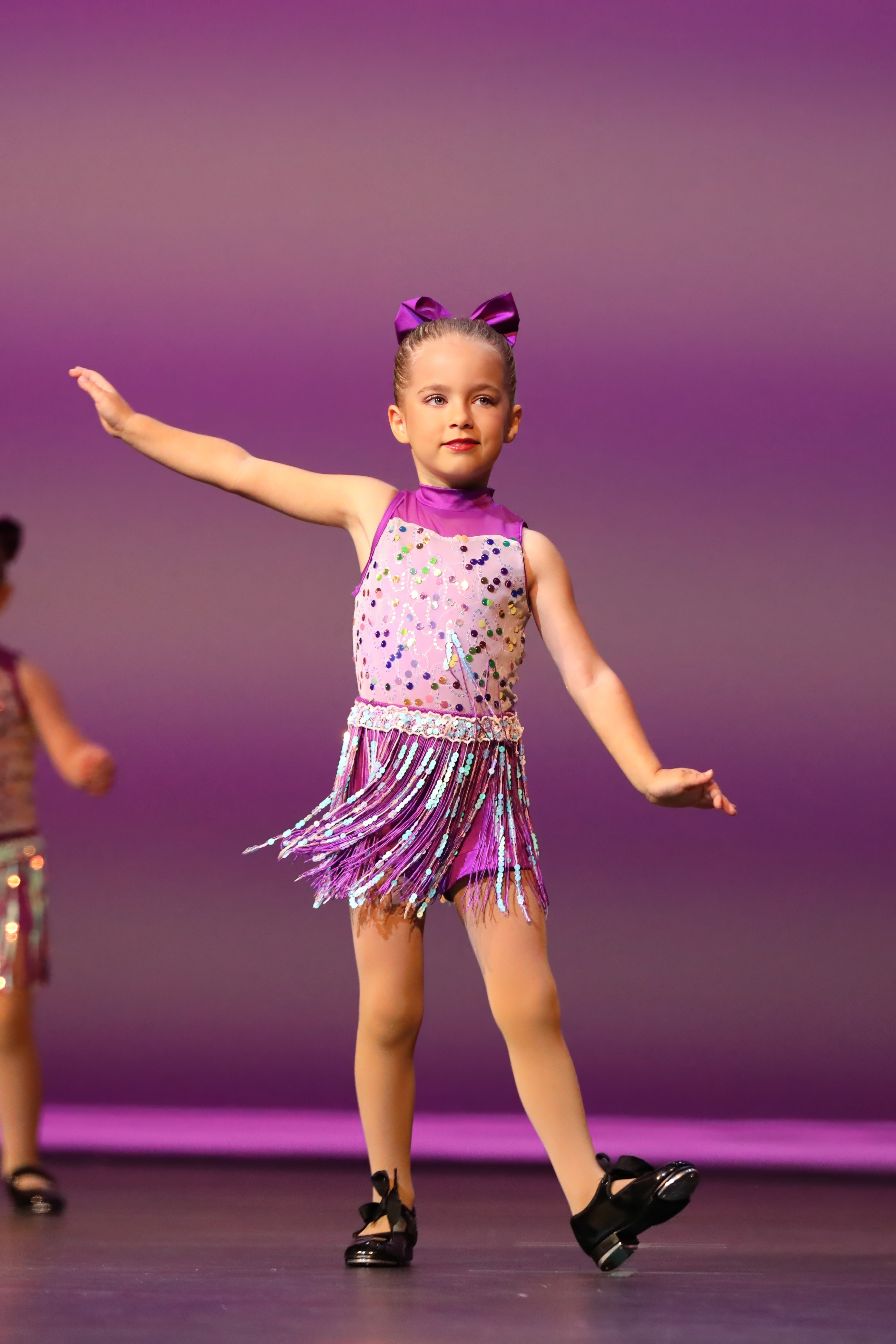 A young girl in a cheerleading outfit poses for a portrait against a black background.