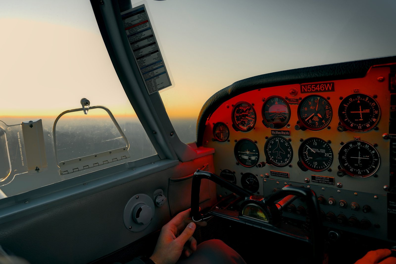 Pilot's hand on the yoke of a training aircraft at sunset
