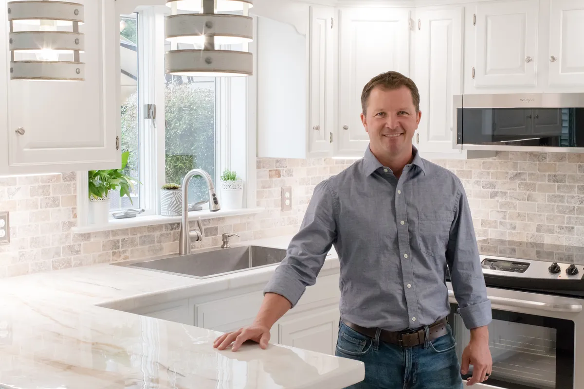 A man is standing and smiling in a newly remodeled kitchen featuring white in Reading, PA by Webster Custom Renovations LLC