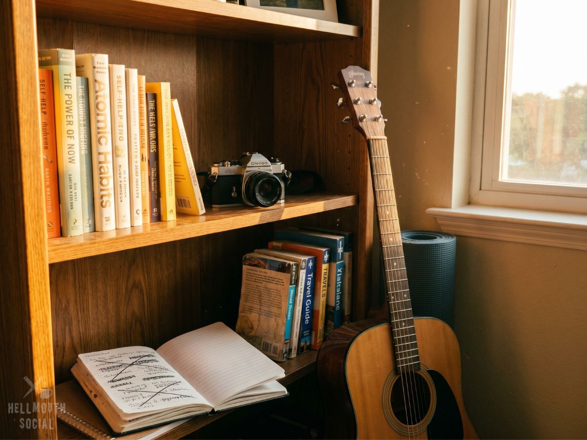 a bookshelf displaying self-help books, a camera, a guitar, a yoga mat, travel guides, and several nearly empty notebooks filled with abandoned plans. Golden-hour light illuminates the collection like artifacts.