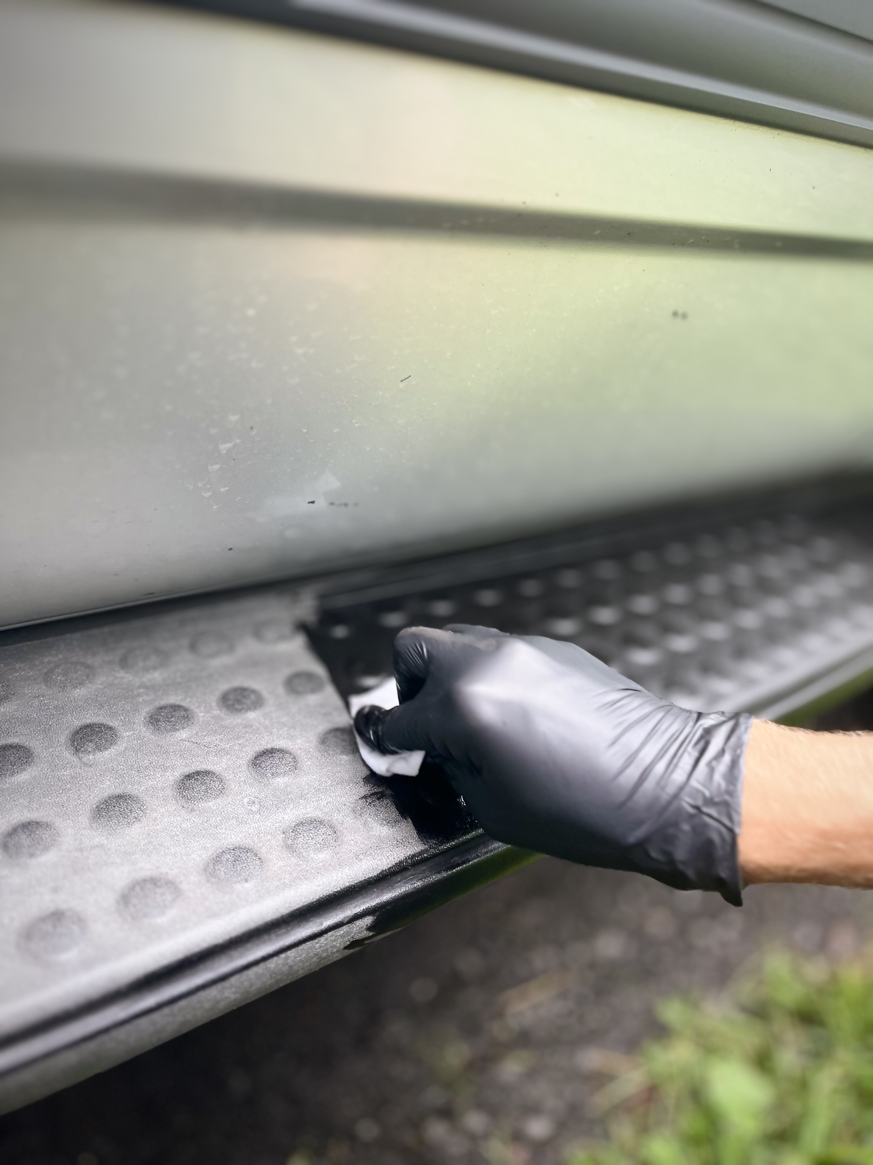 A gloved hand applies dressing to the textured rubber step of a large vehicle's running board or trailer step.