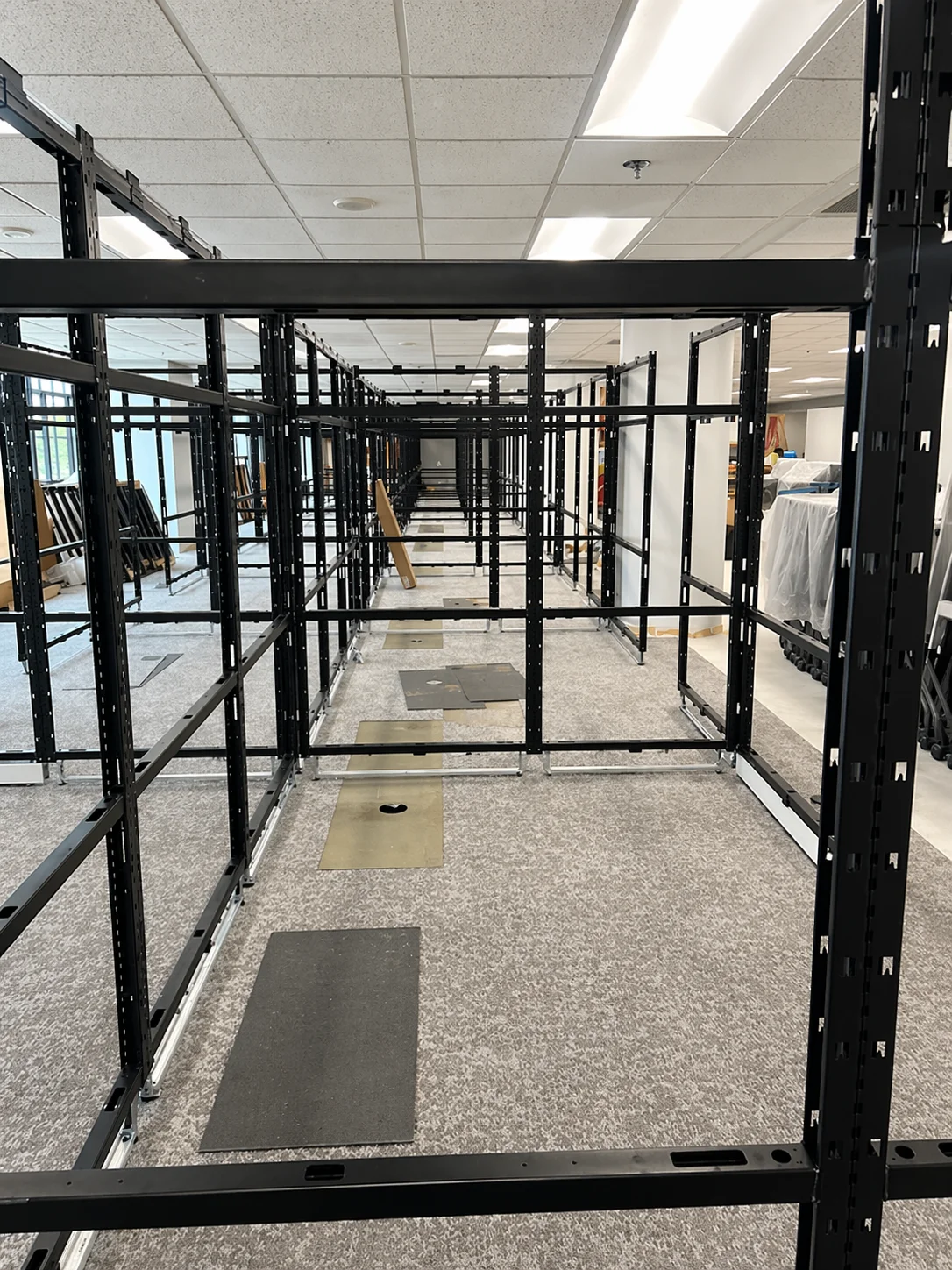 An interior view of a commercial space with black metal framework structures creating aisles, set on a grey carpeted floor.