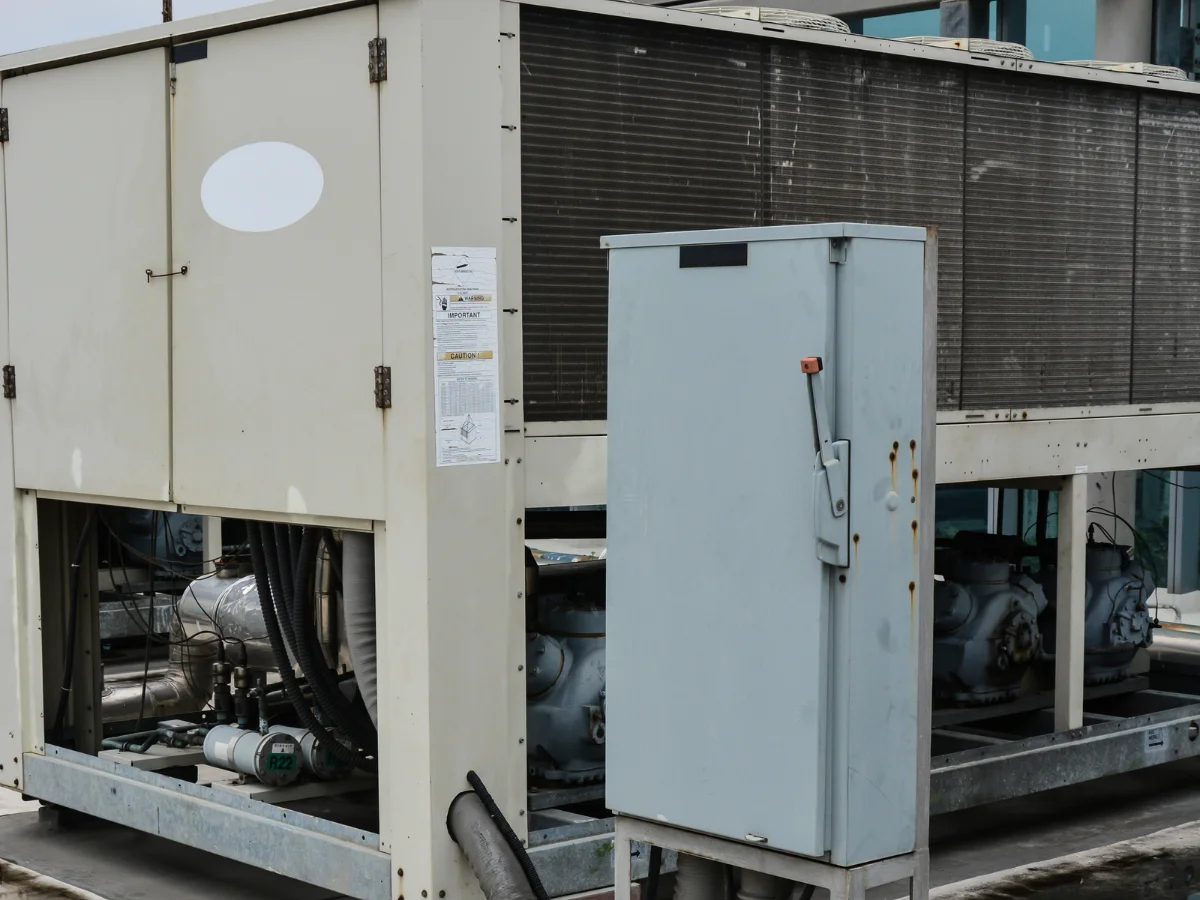 A close-up view of an industrial chiller unit with a control box and exposed machinery against metal fins.