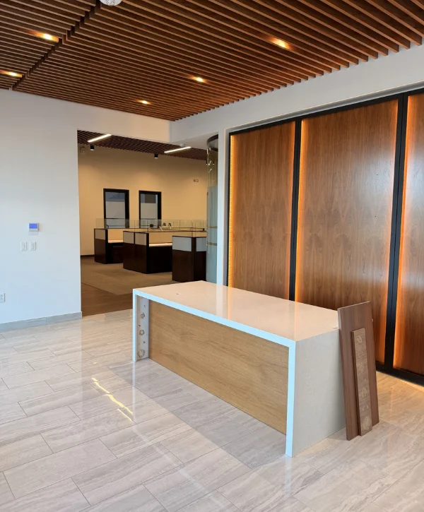 A modern showroom entrance with a light wood and white counter, gray tiled floor, and wooden slat ceiling.