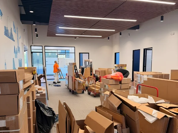 A modern office space filled with moving boxes and two people unpacking items, with a patterned ceiling overhead.