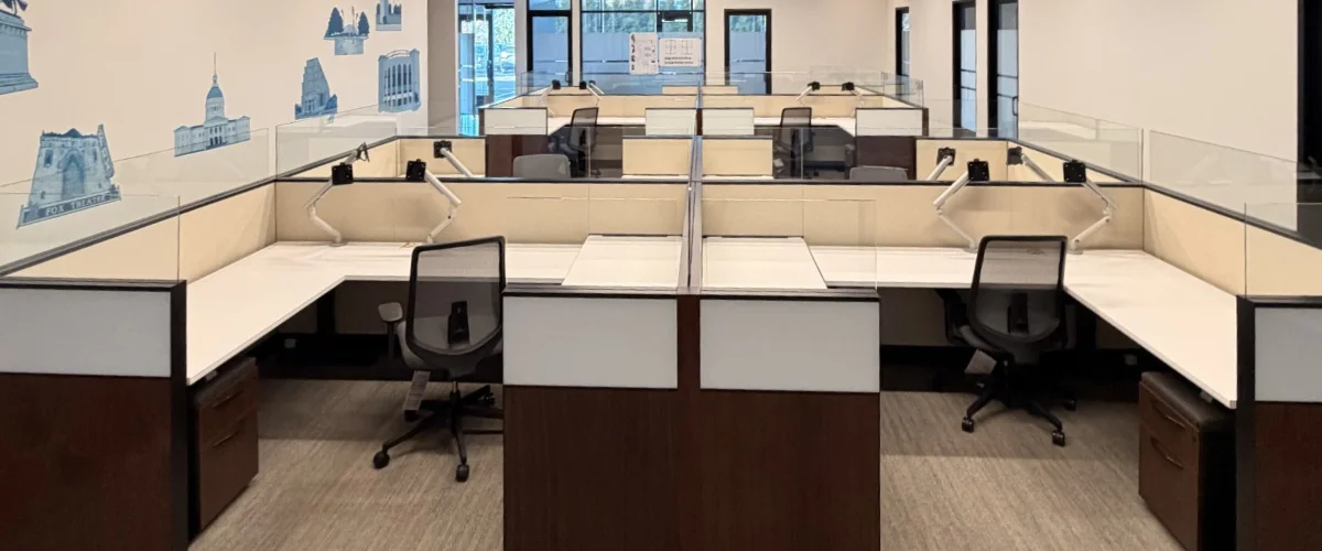 A brightly lit modern office with an empty cubicle layout, featuring blue architectural wall decals. A brightly lit modern office with an empty cubicle layout, featuring blue architectural wall decals.