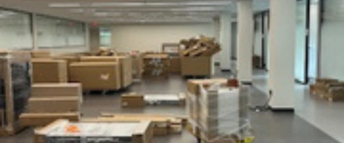 A wide shot of a large office space filled with numerous unpacked cardboard boxes, indicating a recent move or renovation.