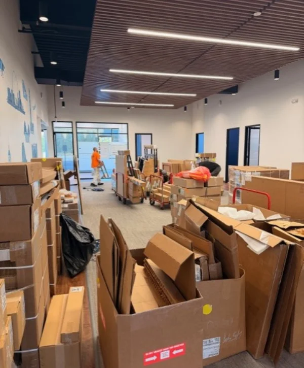 A wide shot of a large office space filled with numerous unpacked cardboard boxes, indicating a recent move or renovation.