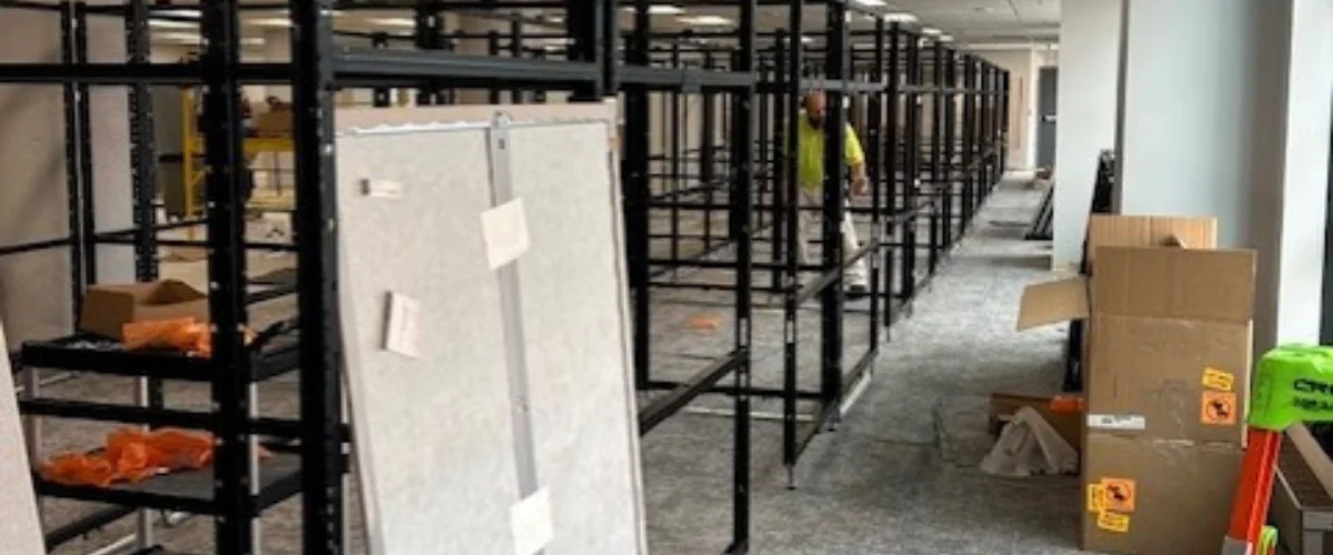 An extensive grid of black metal shelving framework installed on a carpeted floor in a large empty commercial space.