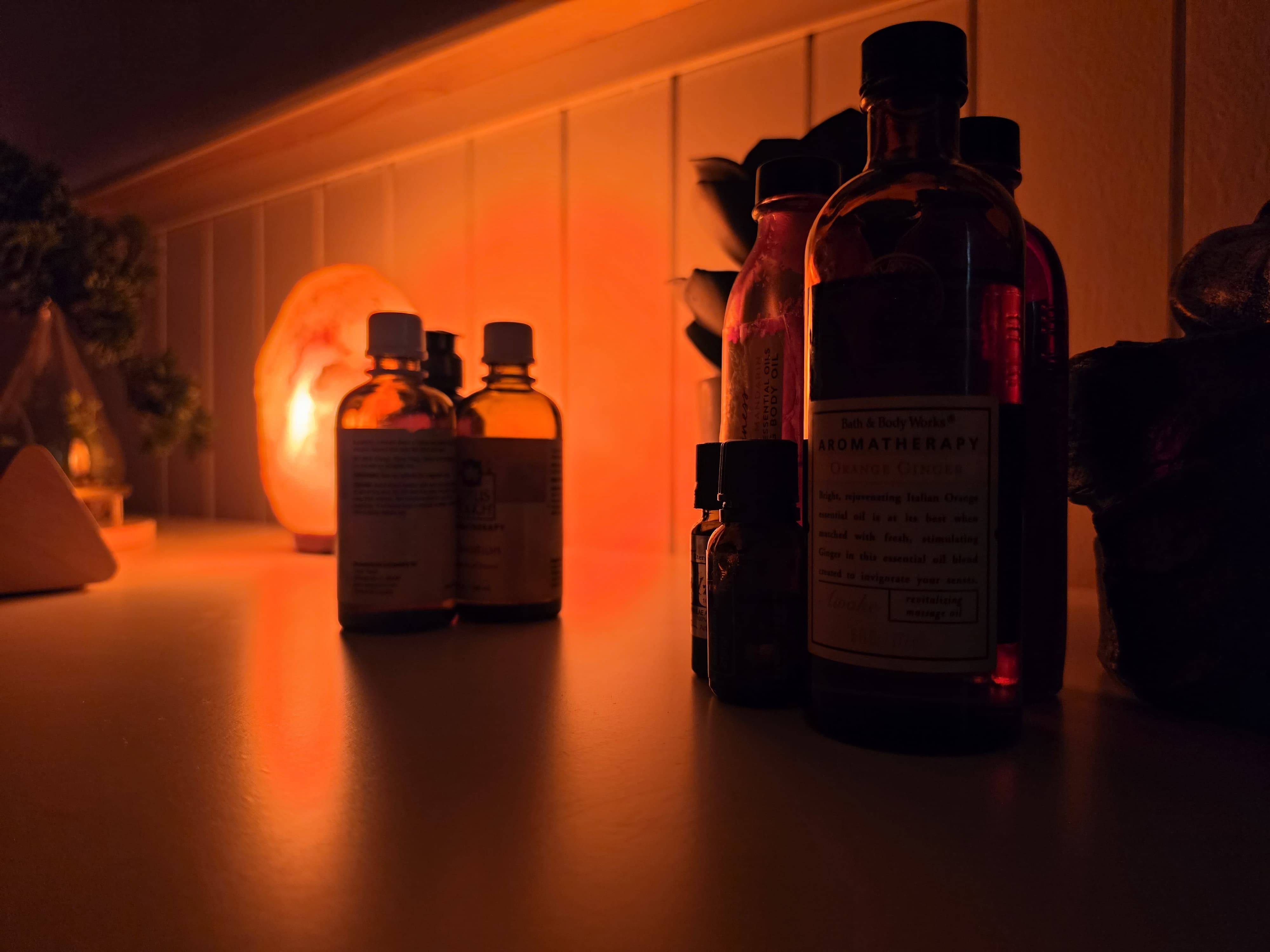 Salt lamp glow across a shelf of oils