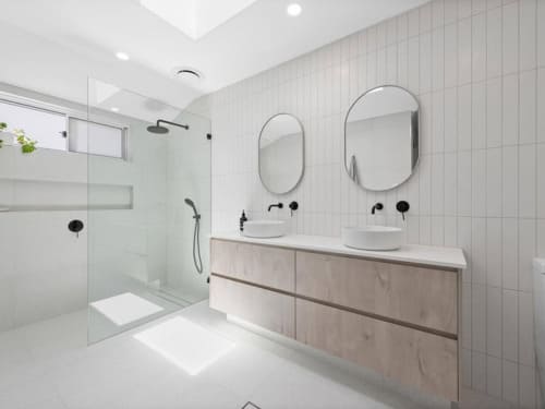 Modern bathroom with double vanity, dual mirrors, black tapware, and natural light