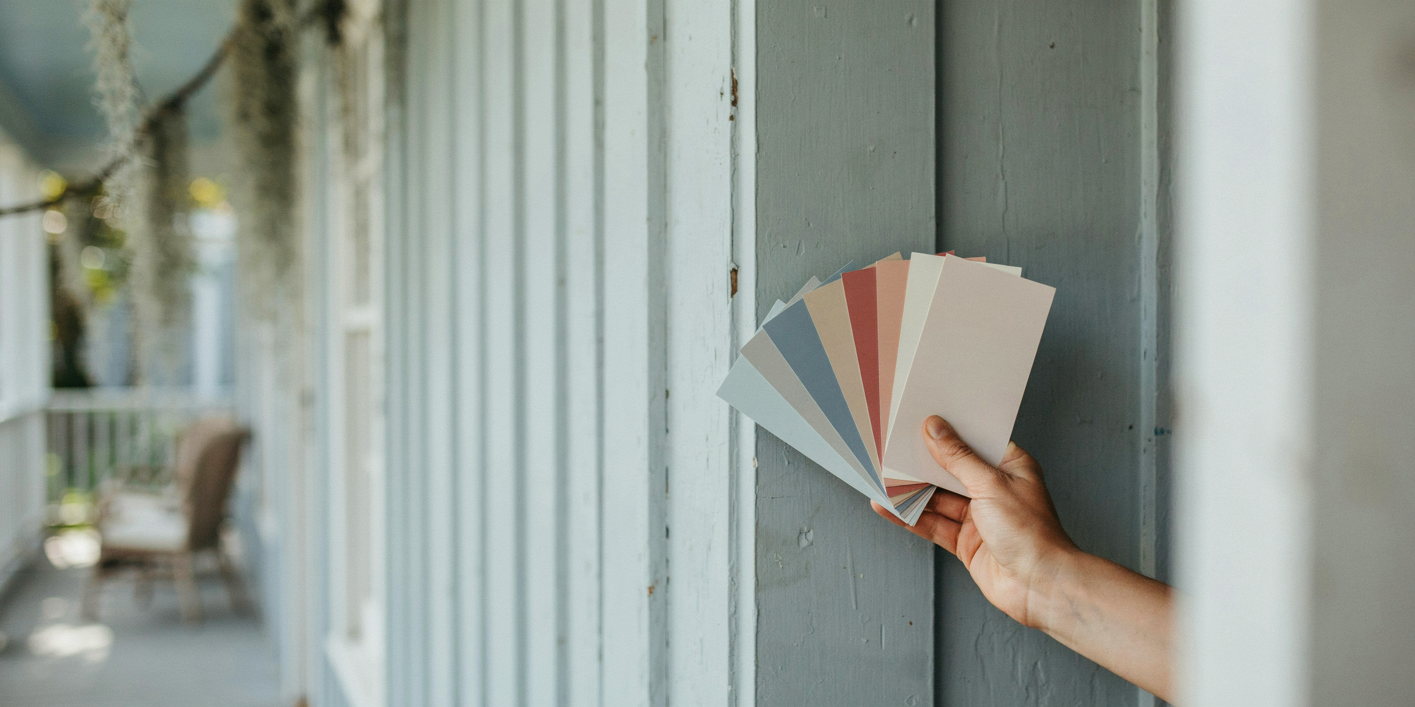 Hand comparing paint swatches against a house exterior