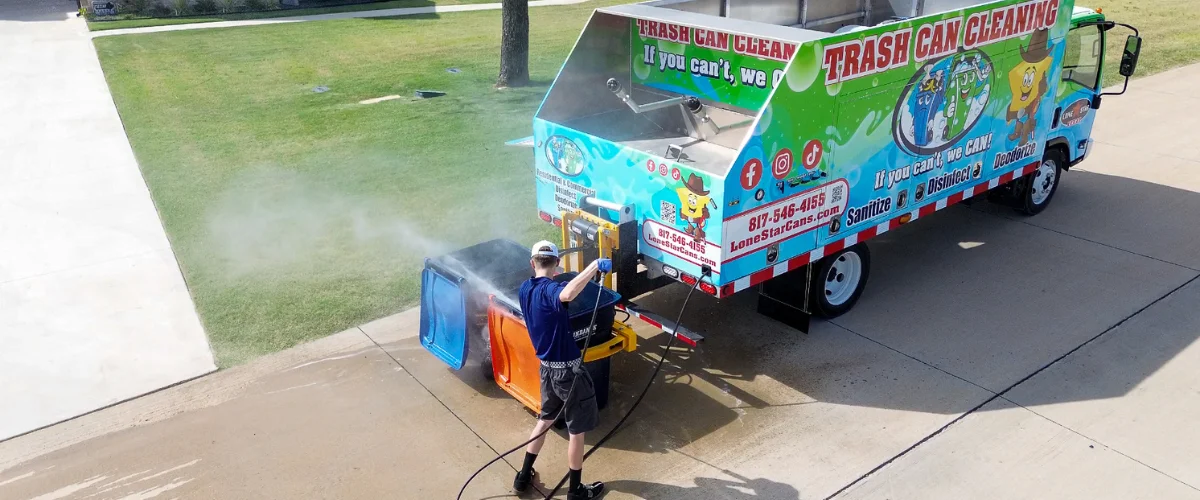 An overhead shot of a man power washing two trash cans next to a vibrant trash can cleaning service truck.