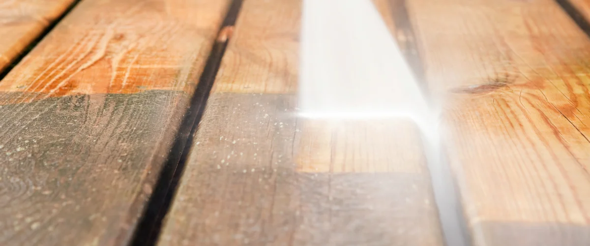 A close-up view of dirty wooden deck planks being sprayed with a powerful jet of water, showing a clean strip emerging. A close-up view of dirty wooden deck planks being sprayed with a powerful jet of water, showing a clean strip emerging.