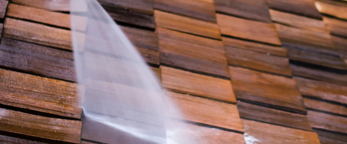 A focused shot of high-pressure water being sprayed onto rustic wooden siding, cleaning it A focused shot of high-pressure water being sprayed onto rustic wooden siding, cleaning it