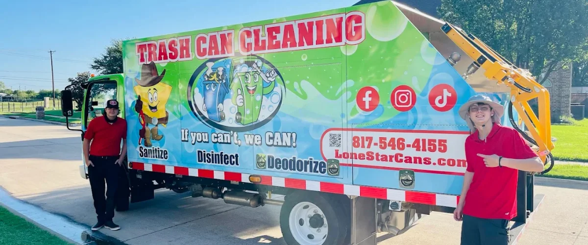 Two men in red shirts standing next to a brightly decorated trash can cleaning truck in a sunny outdoor setting. Two men in red shirts standing next to a brightly decorated trash can cleaning truck in a sunny outdoor setting.