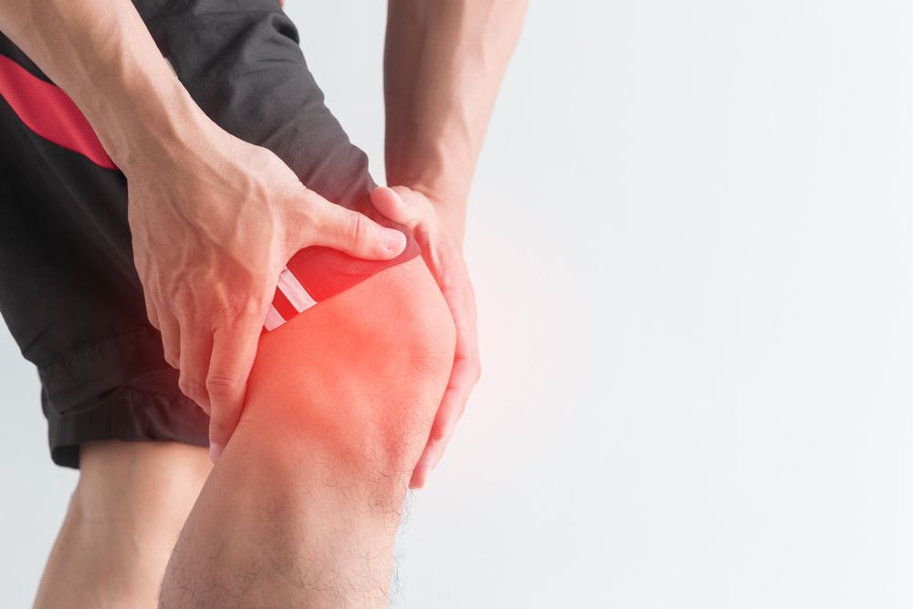 Person holding their knee in pain, with a red highlight indicating discomfort or injury, wearing athletic shorts.