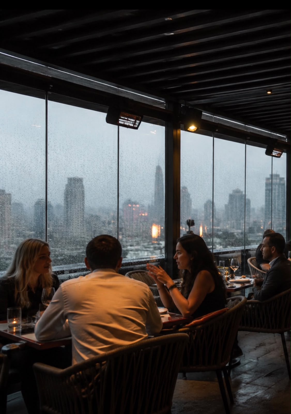 Guests dining on a rooftop during rain beneath a protected pergola