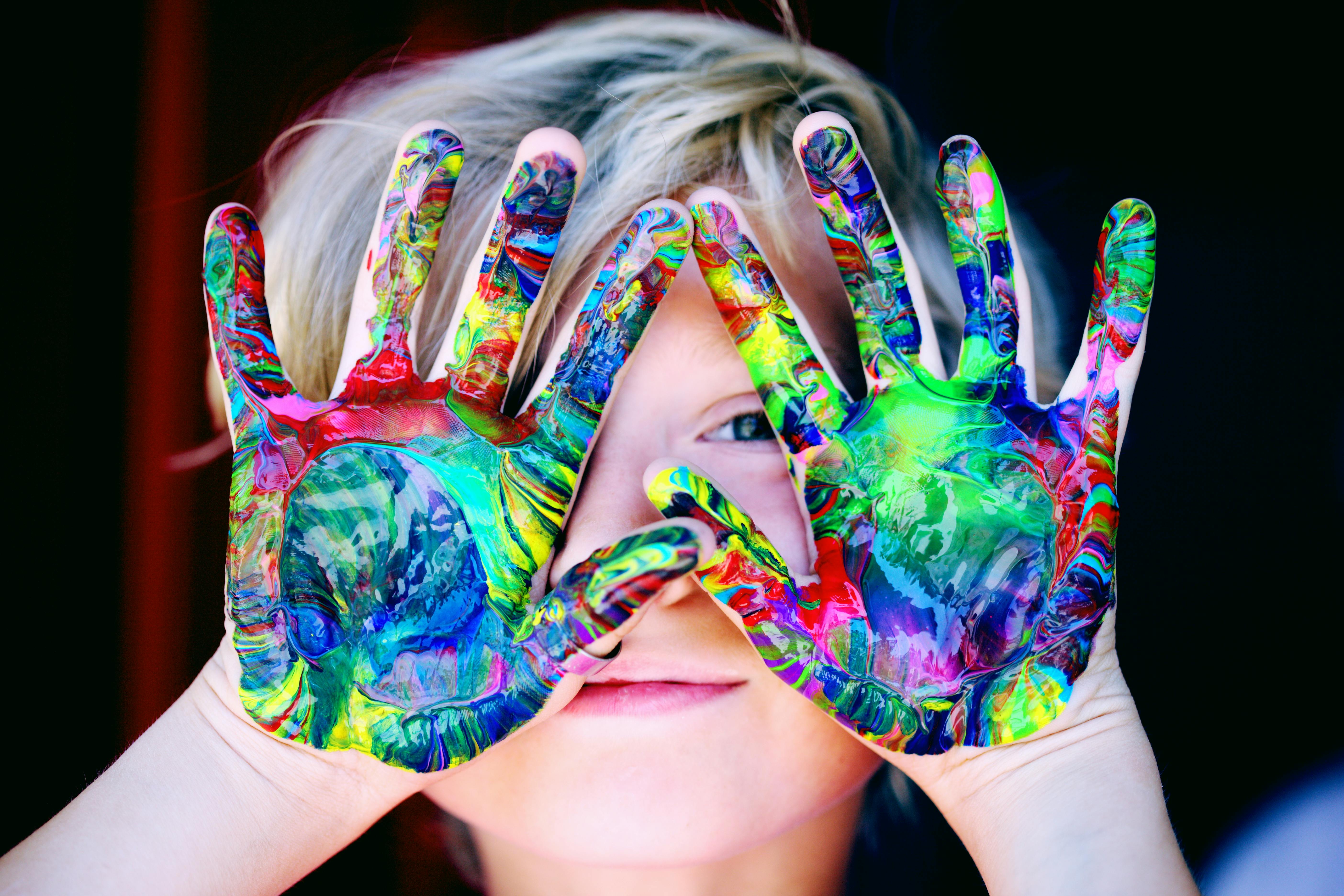 A child with SEND painting their hands in rainbow colours