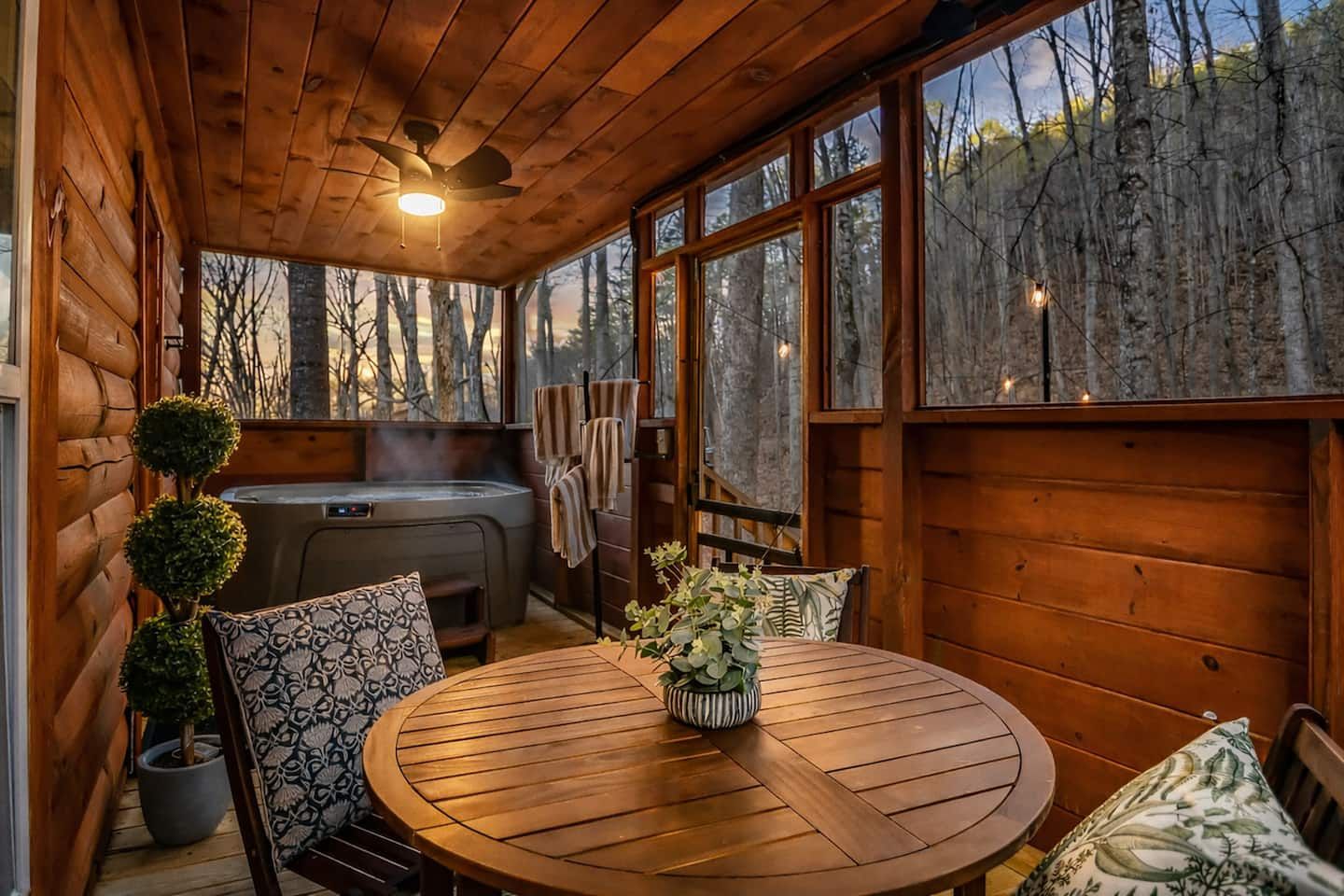 The screened, covered back porch offers a relaxed gathering space — a table for games, meals, or unhurried conversations, all with the quiet backdrop of the woods.