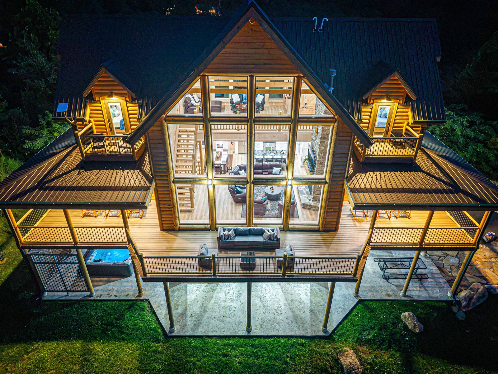 Looking down on the lit cabin, decks, and hot tub at night