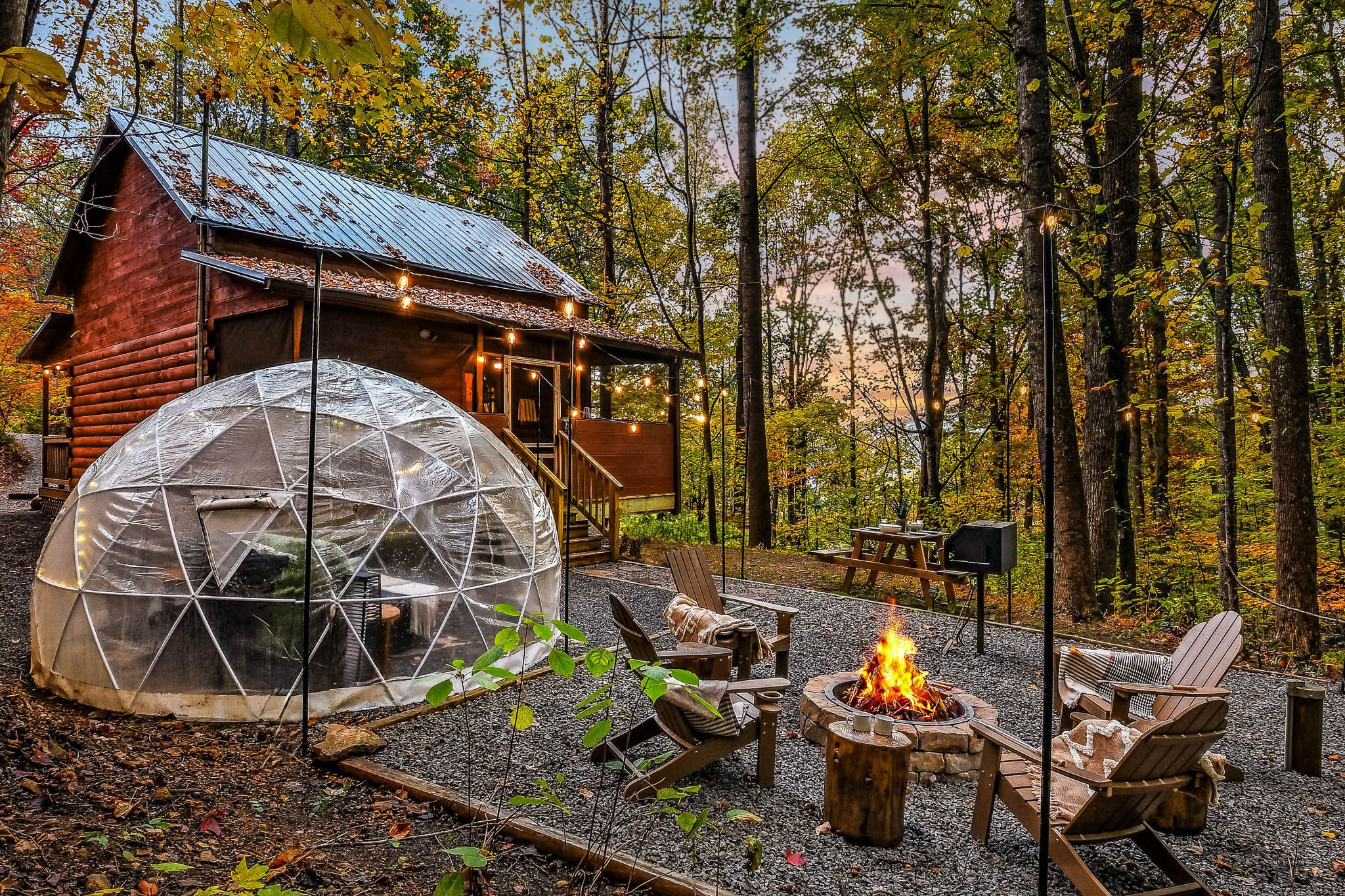 The cozy dome and fire pit beside Bluebird's Perch, string lights glowing at dusk
