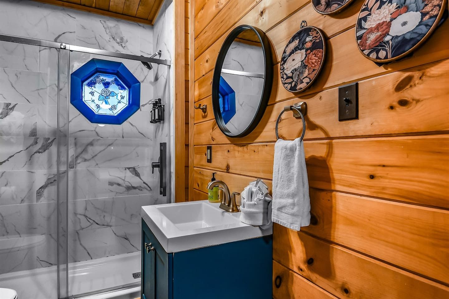 The ensuite bathroom is brightened by a stained glass window, casting soft blue tones that echo the accents throughout the cabin, and adding character and charm to a practical space.