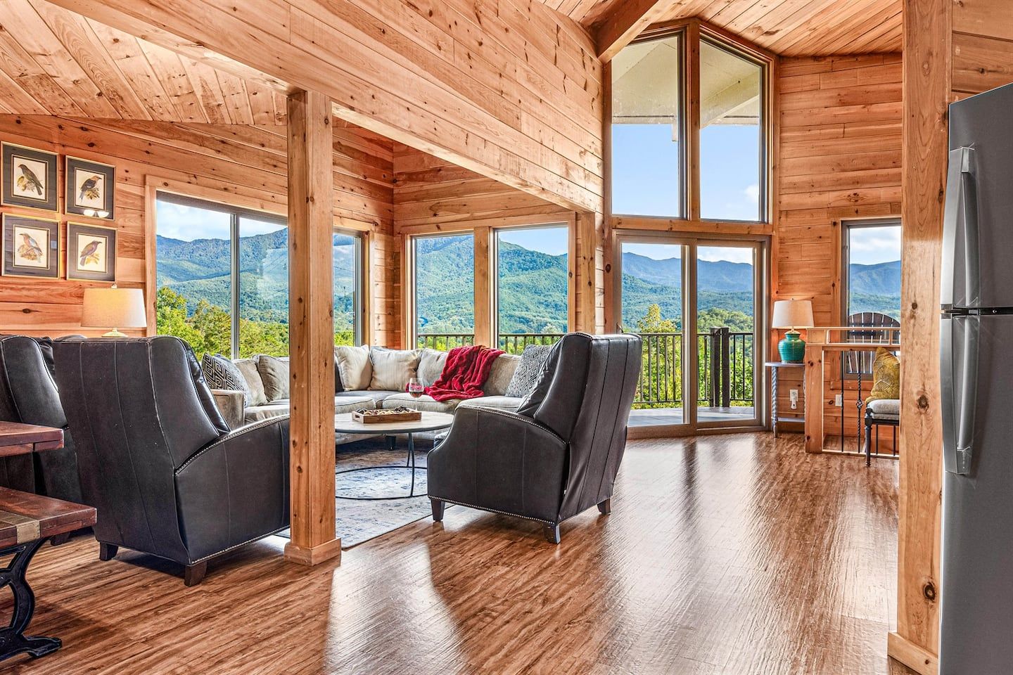 The open-plan living area on the upper level is anchored by a wall of windows and soaring vaulted ceilings. Comfortable seating, warm wood tones, and that view —always the view.