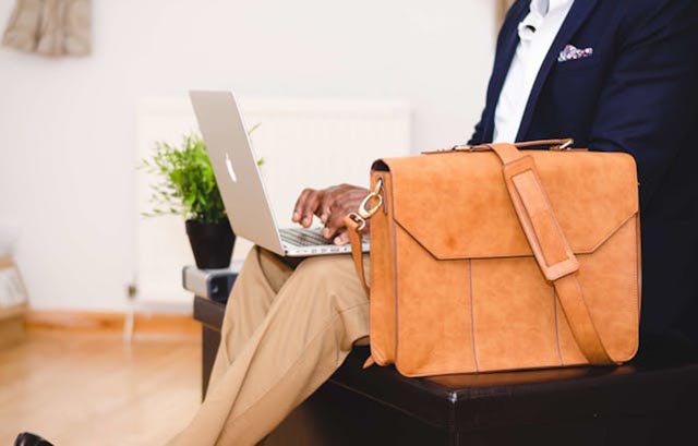 person-sitting-on-a-black-chair-with-a-briefcase-next-to-them-typing-on-a-laptop person-sitting-on-a-black-chair-with-a-briefcase-next-to-them-typing-on-a-laptop