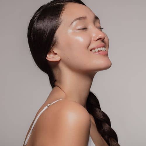 A client in profile with her eyes closed and smiling, her skin clear and evenly lit