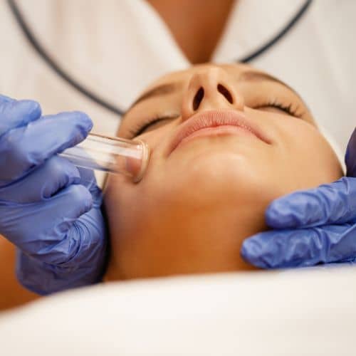 A gloved practitioner working a small glass cup along a client&rsquo;s jaw and neck during a lymphatic drainage session